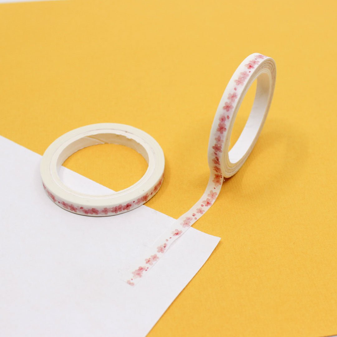 Soft watercolor cherry blossom washi tape roll displayed on a yellow background.