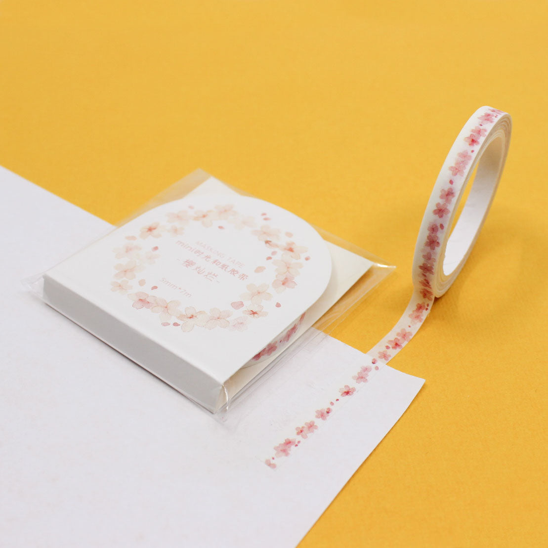 Narrow washi tape with pink cherry blossom petal pattern unrolled on journal paper.