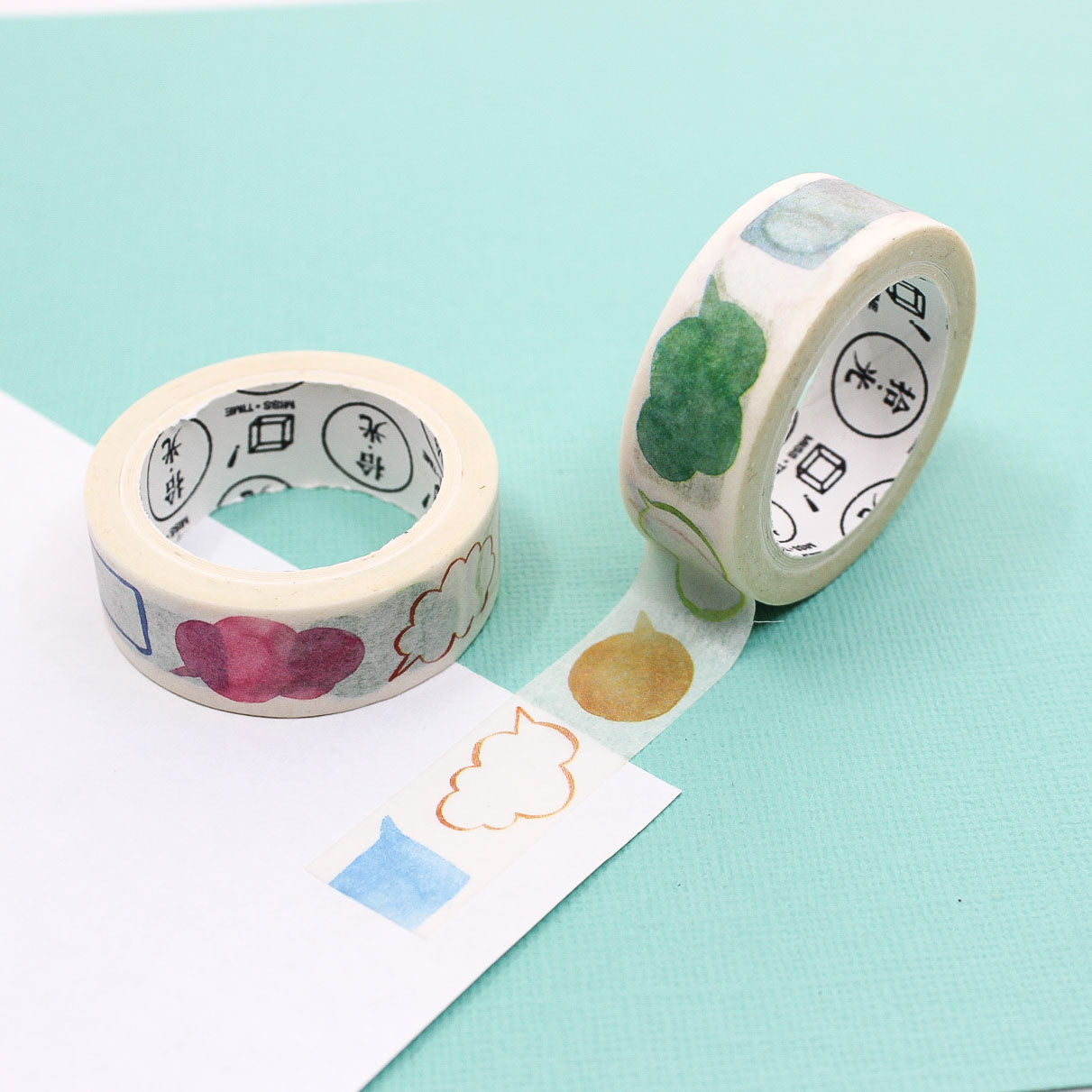 Pastel watercolor shapes washi tape roll beside its matching box on a mint background.