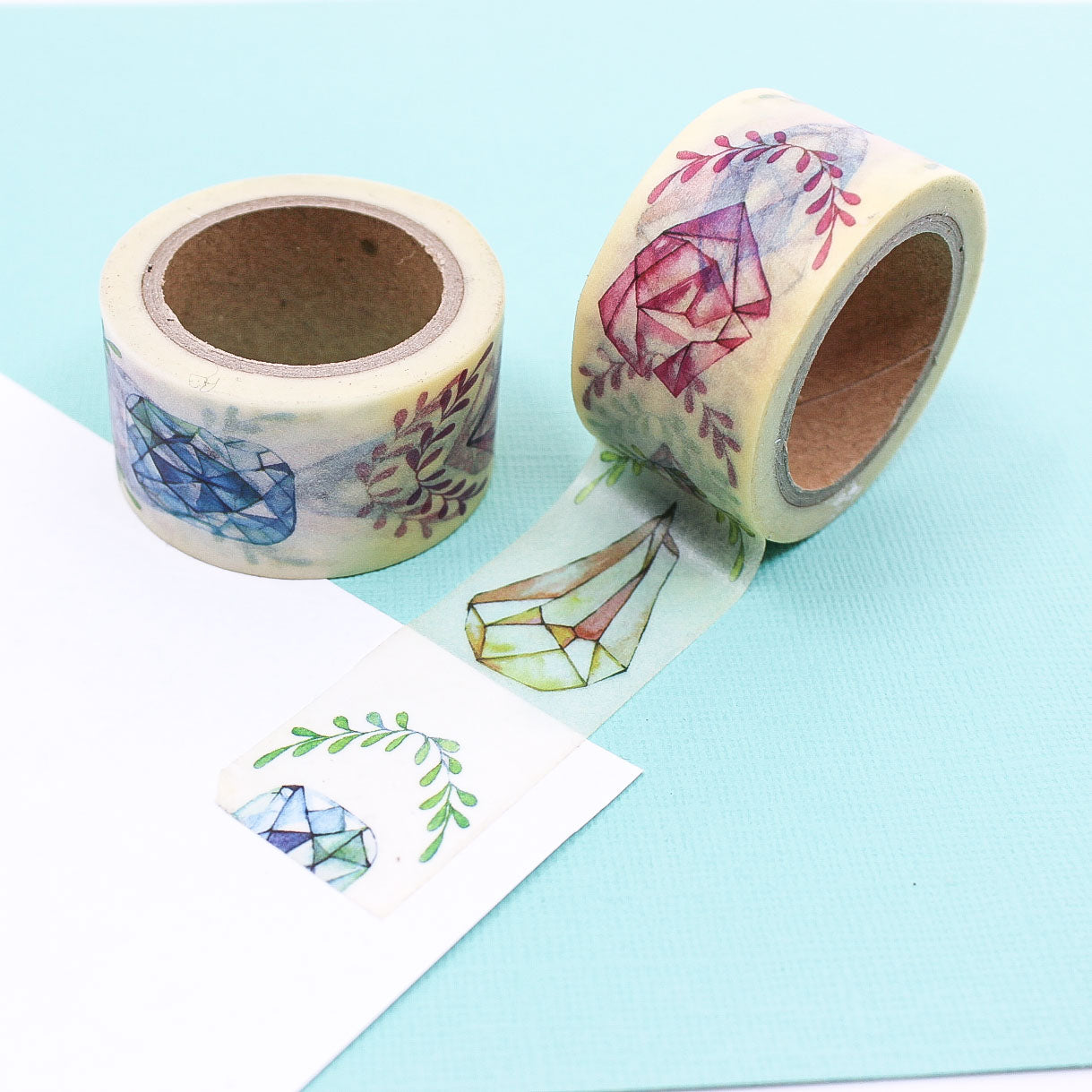 Washi tape roll with watercolor gemstones and leafy branches pattern on a pastel background.