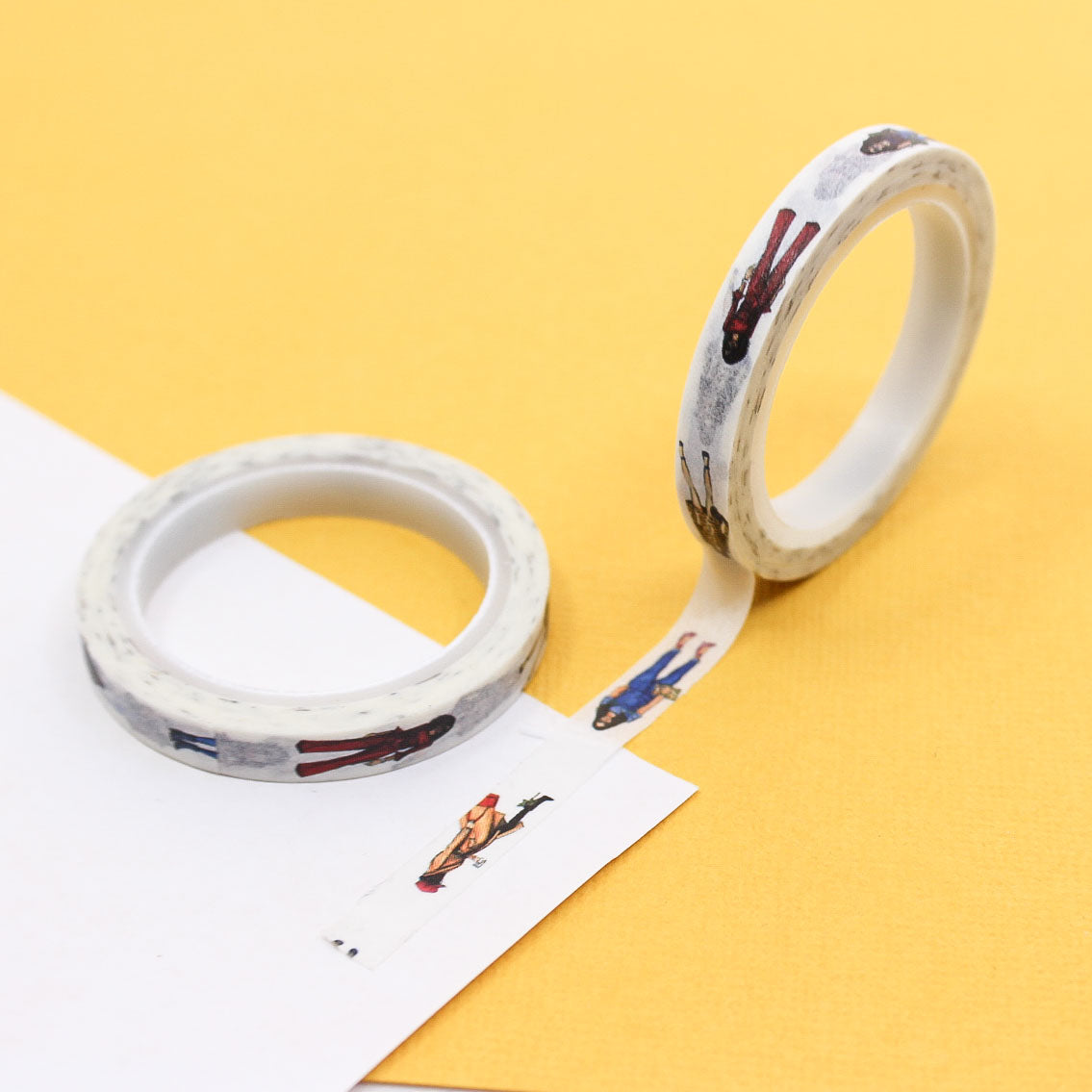 Narrow washi tape with tiny illustrated fashion people rolled out on journal paper.