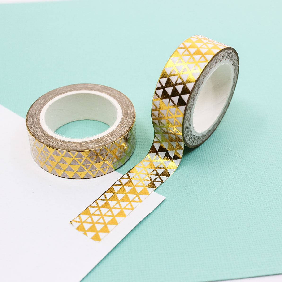 Gold foil triangle washi tape roll unrolled on a mint background.