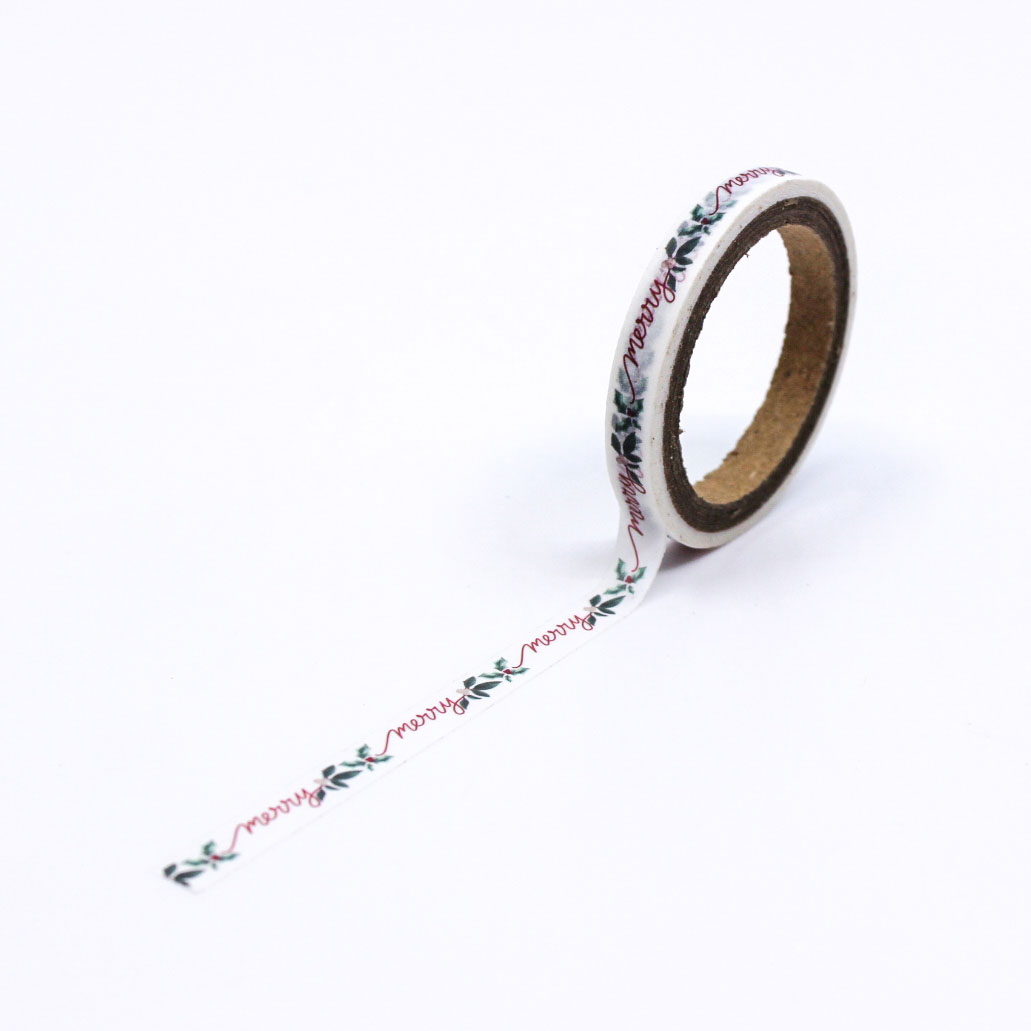 Merry script washi tape unrolled on white paper showing festive pattern.