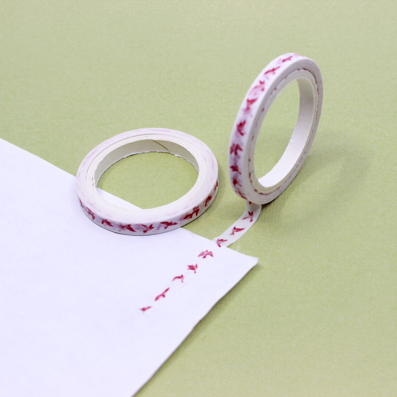 Narrow washi tape with small pink birds rolled out on white paper against a green background.
