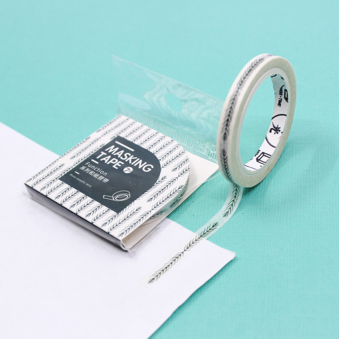 Thin olive leaf patterned washi tape rolled out across white journal paper on a teal background.