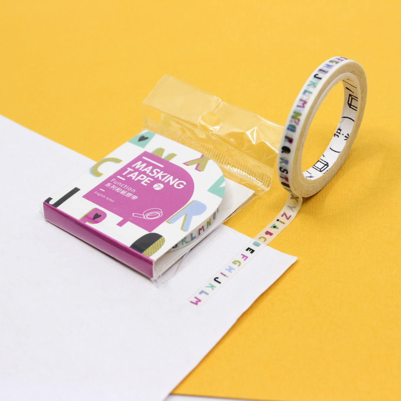Narrow alphabet washi tape roll unrolled to show tiny colorful letters on white tape.