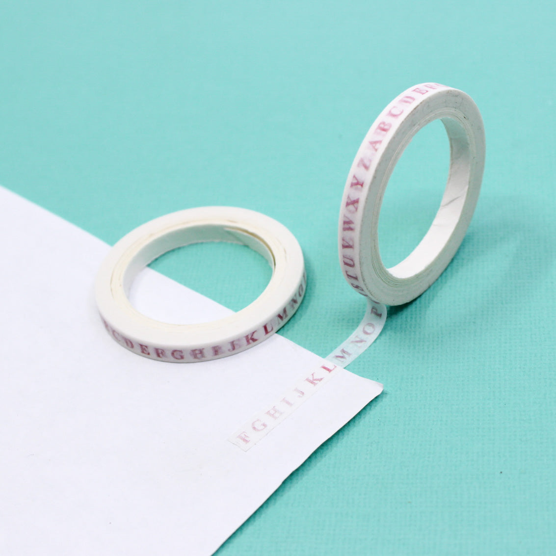Close-up of serif pink letter pattern on thin white washi tape.
