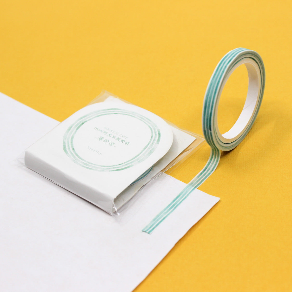 Narrow mint stripe washi tape roll unspooled on white paper.