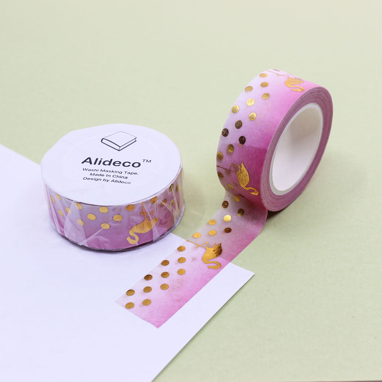 Pink gradient washi tape with gold foil flamingos and polka dots unrolled on paper.