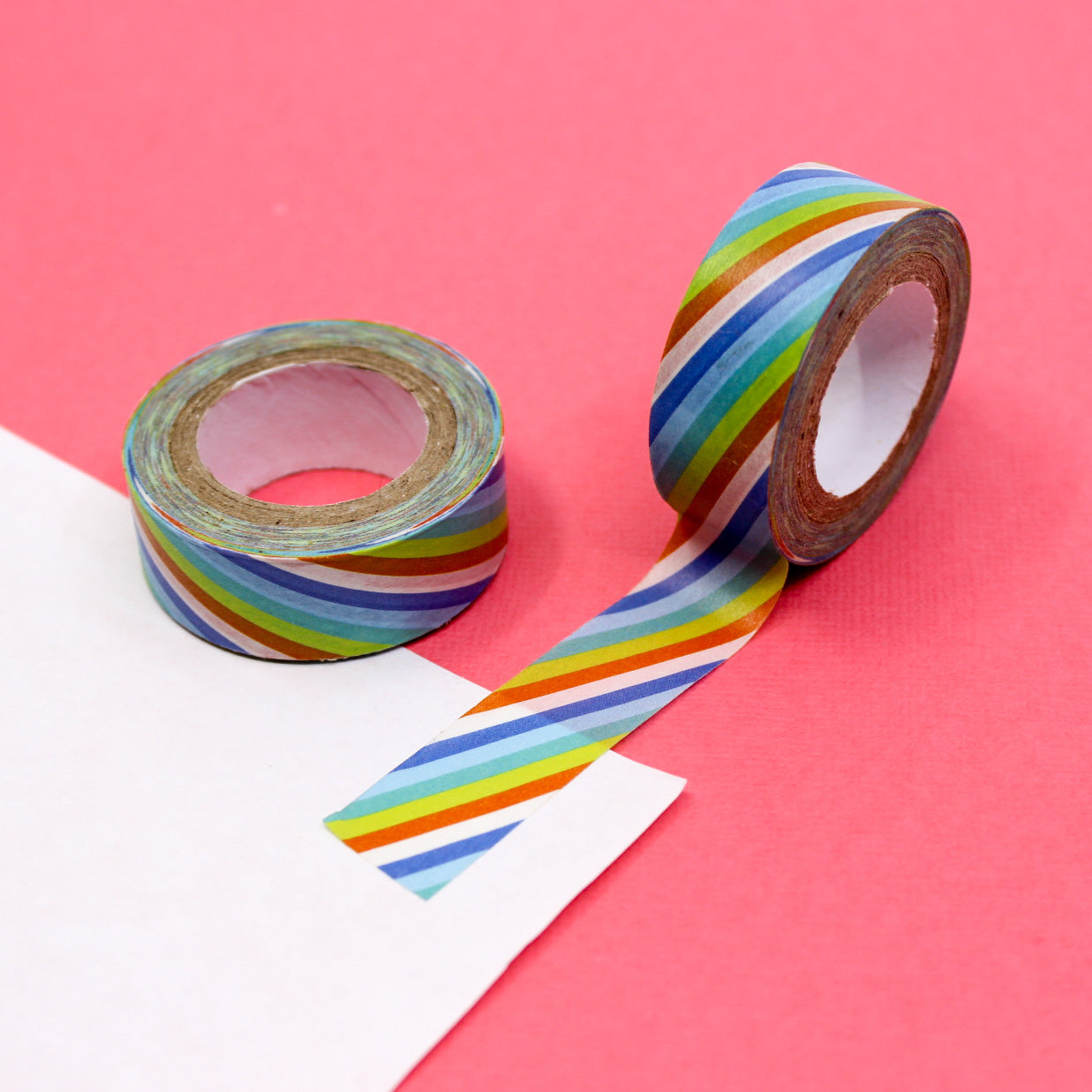 Rainbow washi tape unrolled on white paper against a pink background.
