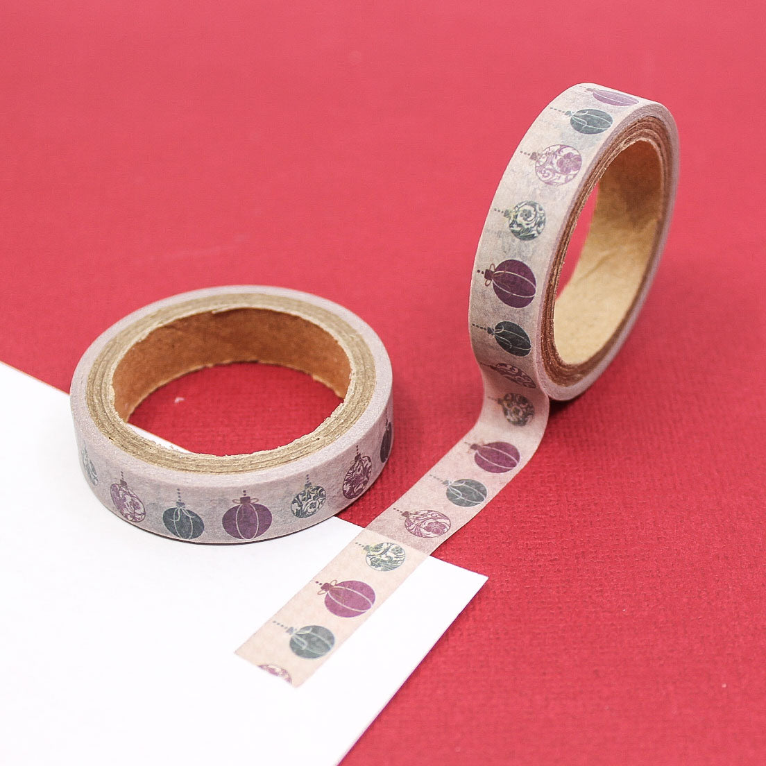 Roll of vintage ornament washi tape unrolled on red background showing bauble pattern.