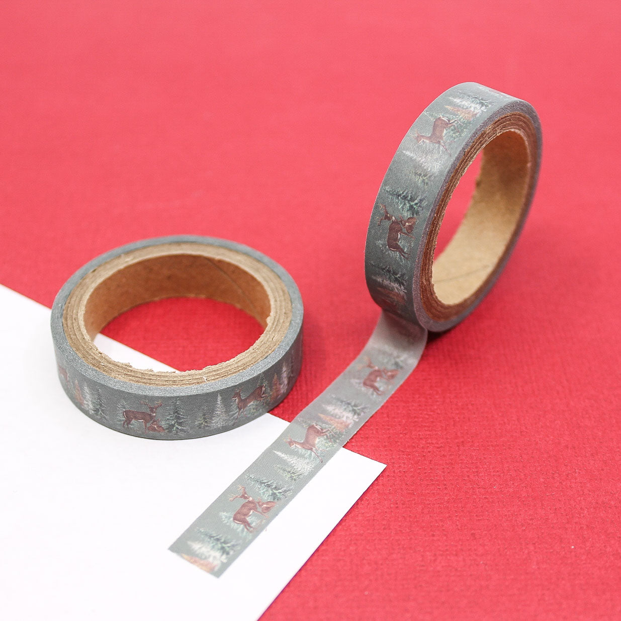 Narrow washi tape with deer and pine tree forest design on a gray background.