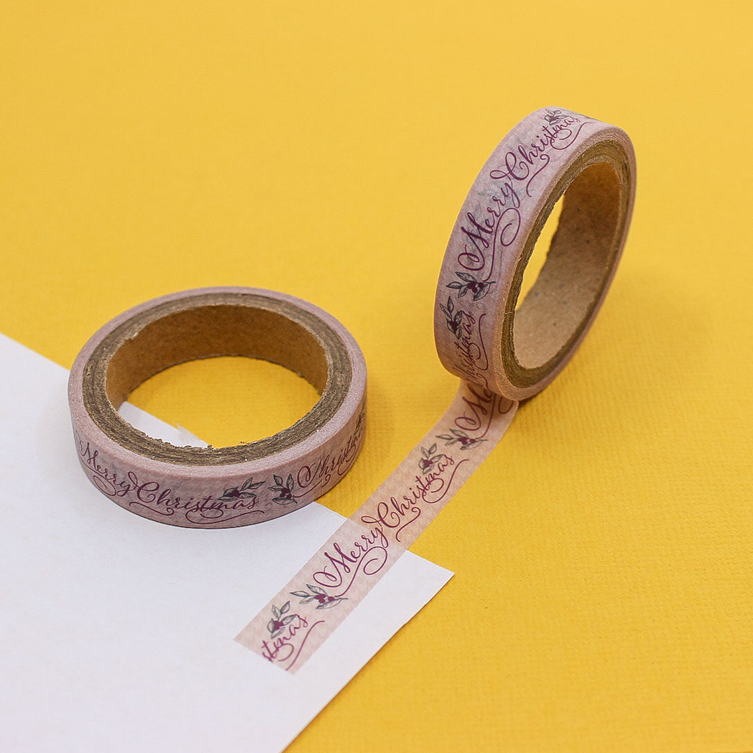 Narrow washi tape with Merry Christmas cursive lettering and holly leaves on soft pink background.
