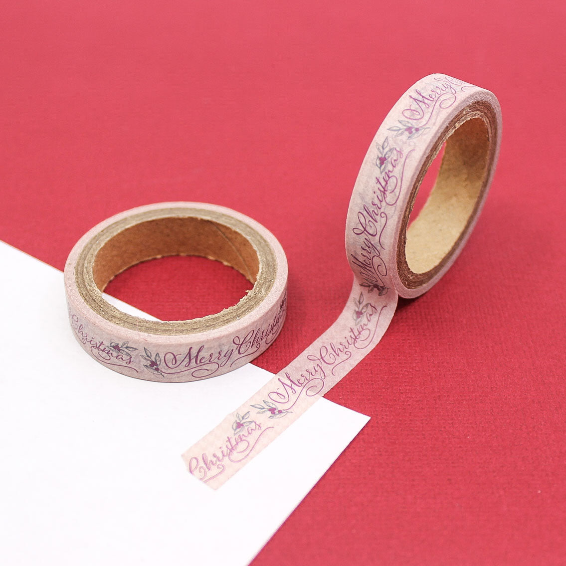 Narrow washi tape with Merry Christmas cursive lettering and holly leaves on soft pink background.