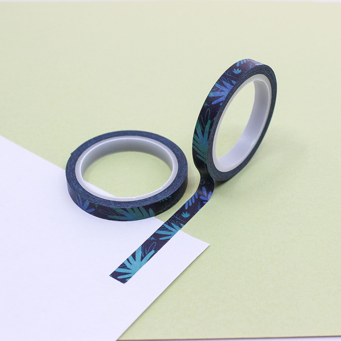 Dark botanical washi tape with teal leaves rolled out on paper.