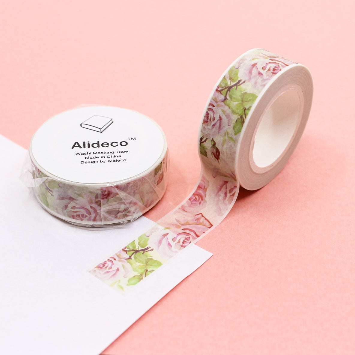Watercolor rose washi tape roll unrolled on pink background showing floral pattern.