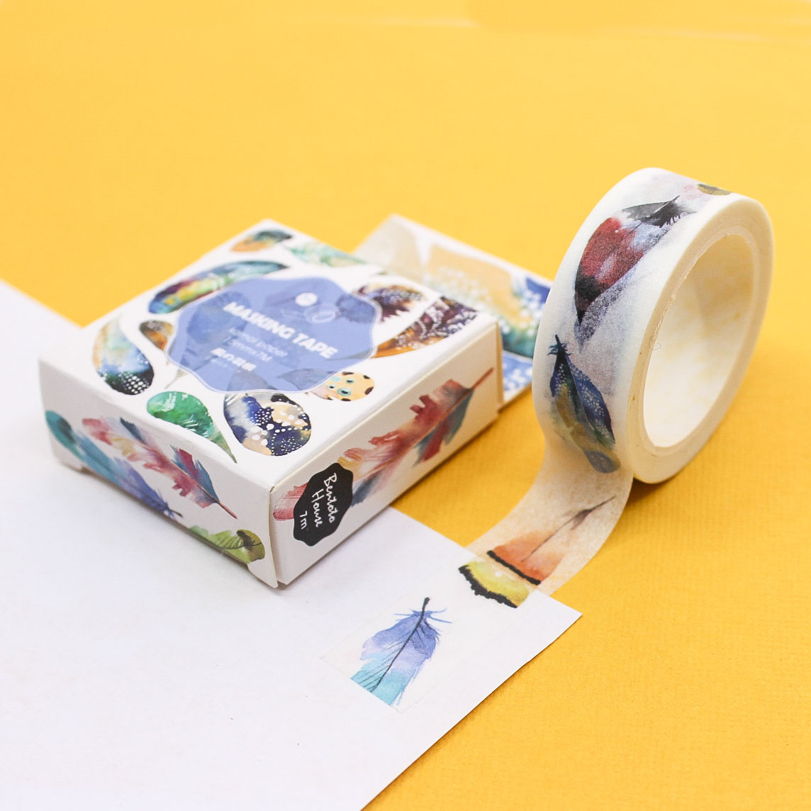 Watercolor feather washi tape roll and packaging displayed on yellow background.