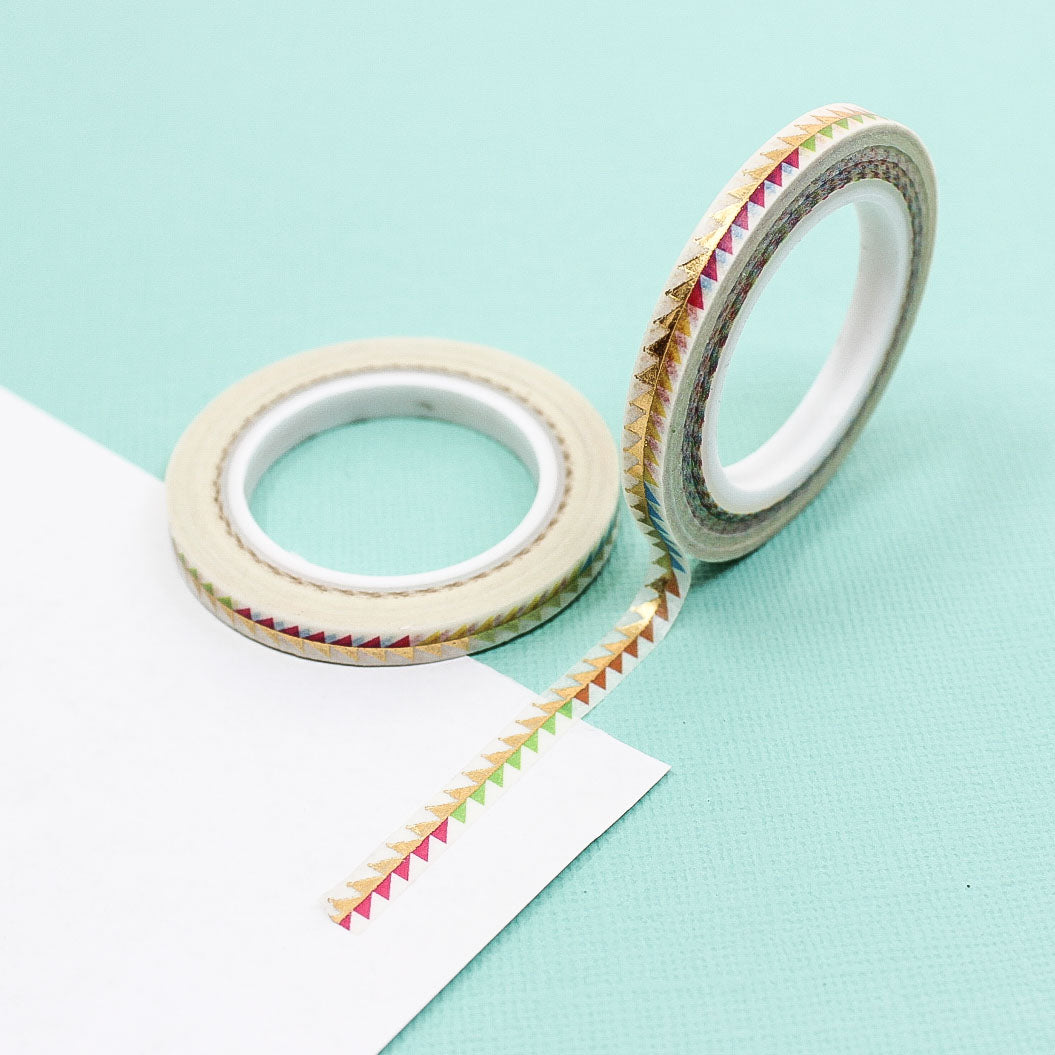 Narrow washi tape with colorful foil triangles rolled out on paper.