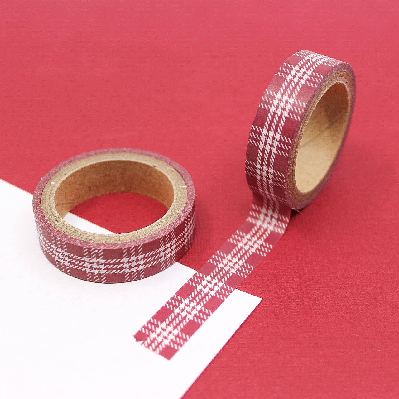 ed plaid washi tape roll unrolled on white paper against red background.