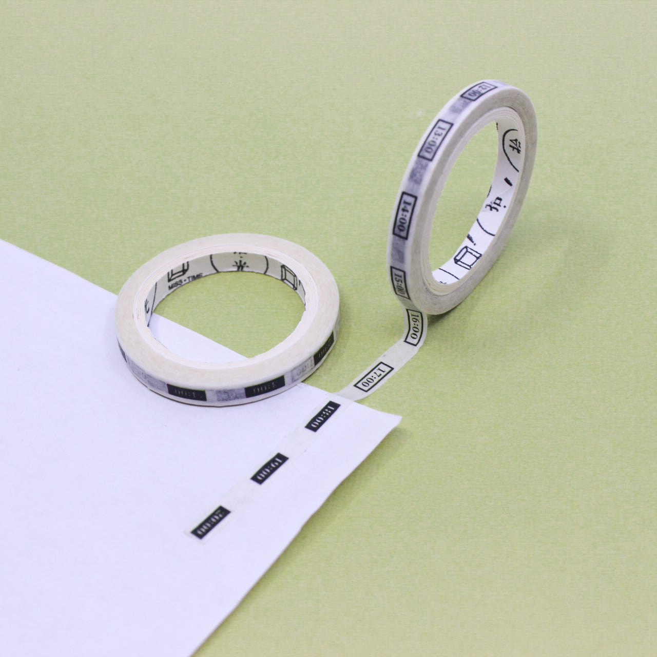 Narrow planner washi tape roll with black-and-white hourly time labels unrolled on paper.
