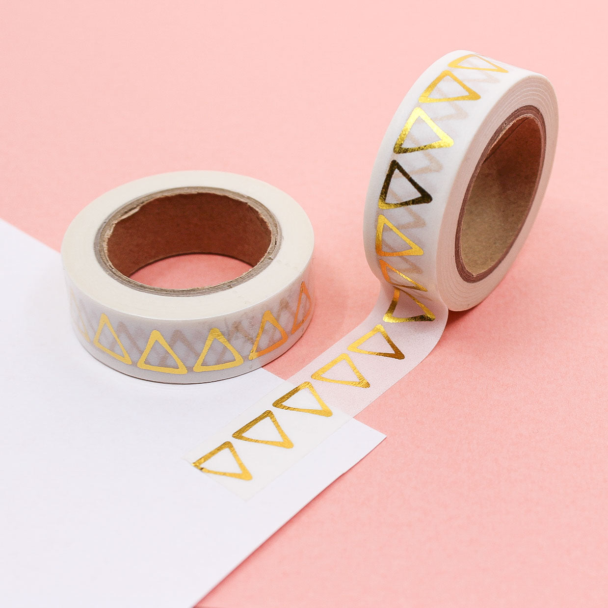 Gold geometric triangle washi tape roll with marble background, unrolled on pink paper.