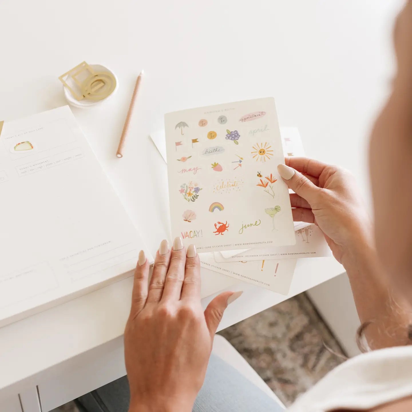 Person holding these seasonal sticker sheet on a desk she is going to use in her planner.
