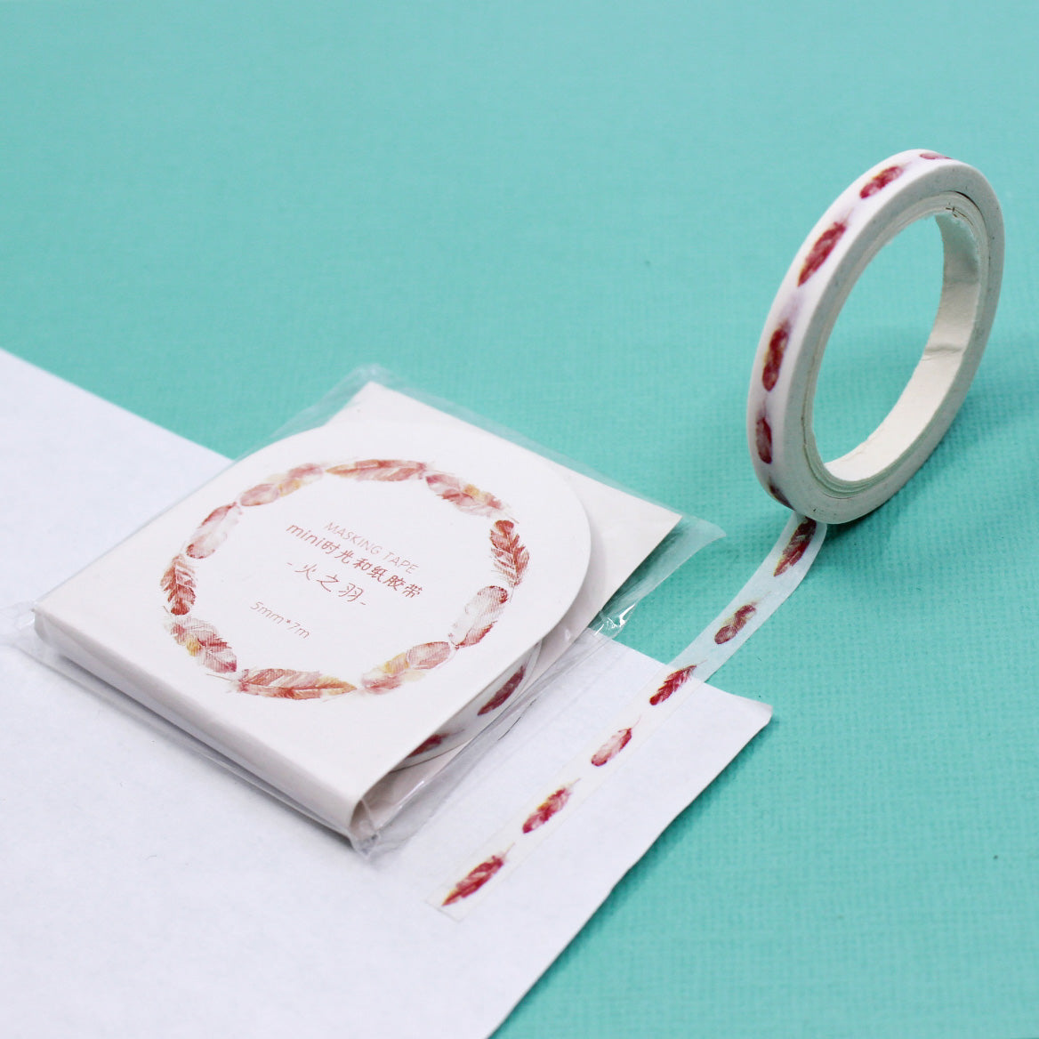 Narrow washi tape with watercolor feathers unrolled on paper.