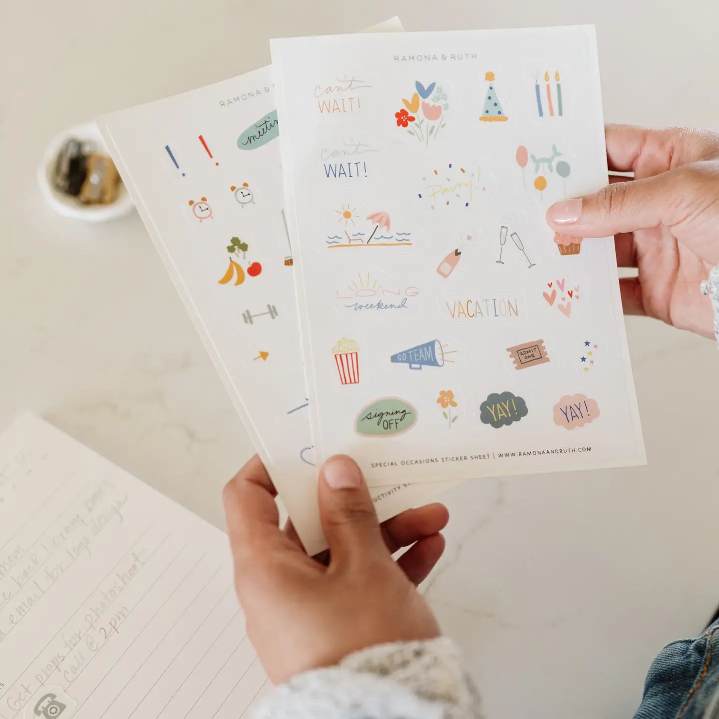 Two sheets of decorative stickers held by a person that feature Illustrated party and celebration planner sticker set